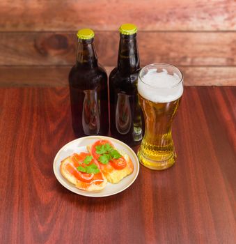 Two different bottles and glass of the lager beer and two sandwiches made with a salted trout on the saucer on the dark red wooden table 
