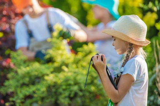 Children and the Internet. Little Girl Playing with Her Tablet Device in the Garden While Parents Working in the Background. Parental Control Conceptual Photo.