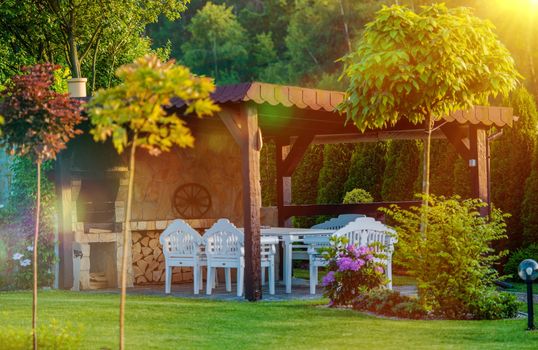Outdoor Garden BBQ Area. Garden Grilling Place with Fireplace and White Garden Furnitures.