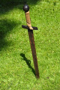 Old rusty sword on green grass background