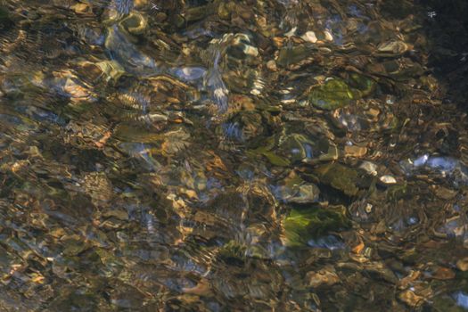 River floor, texture. Pebbles underwater in sunlight.