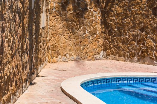 Luxury swimming pool with beautiful landscaping of the territory. In the background a mediterranean wall decorated with sandstones.