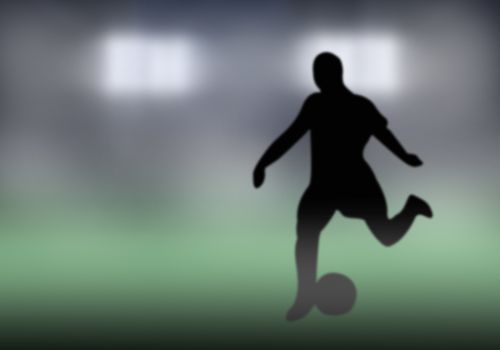 Silhouette of soccer player kicking the ball out in front.