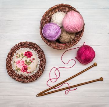 From above the colored balls of yarn in wicker basket with needles on white wooden board in Ukraine