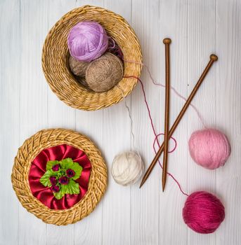 From above the colored balls of yarn in wicker basket with needles on white wooden board in Ukraine