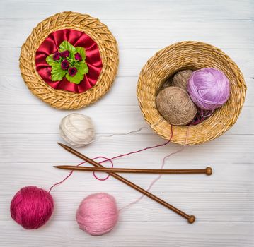 From above the colored balls of yarn in wicker basket with needles on white wooden board in Ukraine
