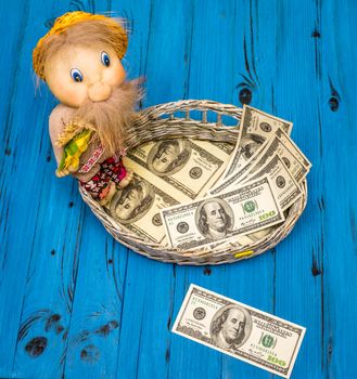 From above few dollar bills in a wicker basket and one hundred dollars bill on board with traditional toy of man on a blue wooden board in Ukraine.