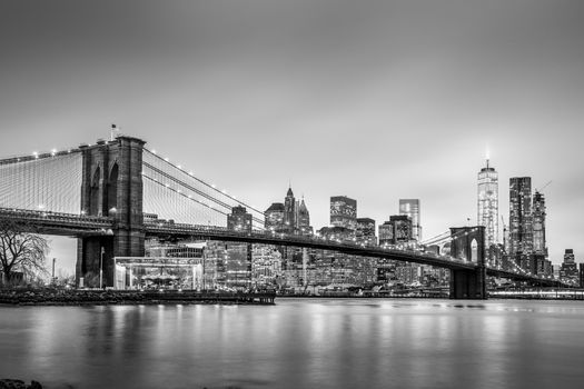 Brooklyn bridge and New York City Manhattan downtown skyline at dusk with skyscrapers illuminated over East River panorama. Panoramic composition.