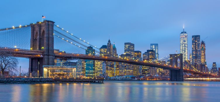 Brooklyn bridge and New York City Manhattan downtown skyline at dusk with skyscrapers illuminated over East River panorama. Panoramic composition.