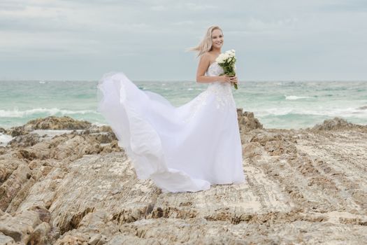 Beautiful bride at the beach with a flower bouquet.
