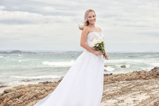 Beautiful bride at the beach with a flower bouquet.