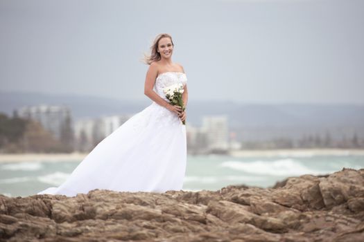 Beautiful bride at the beach with a flower bouquet.