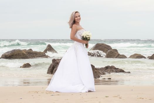 Beautiful bride at the beach with a flower bouquet.