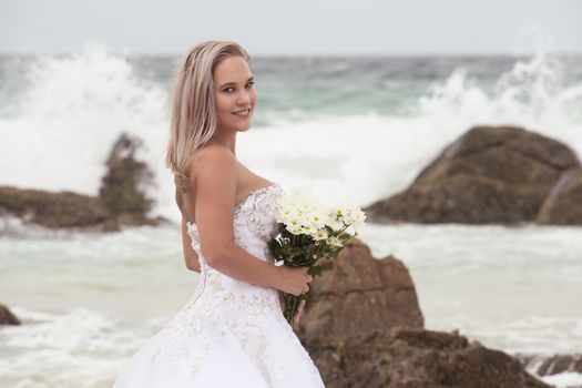 Beautiful bride at the beach with a flower bouquet.