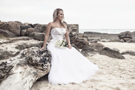 Beautiful bride at the beach with a flower bouquet.