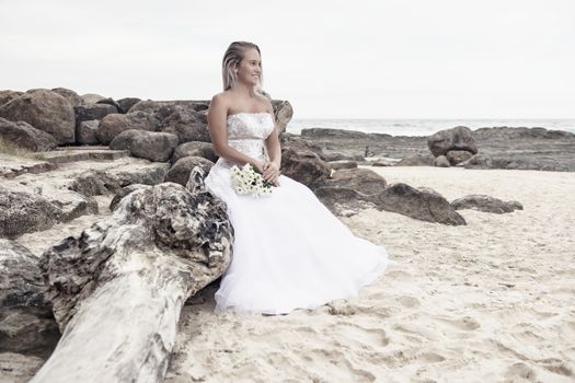 Beautiful bride at the beach with a flower bouquet.