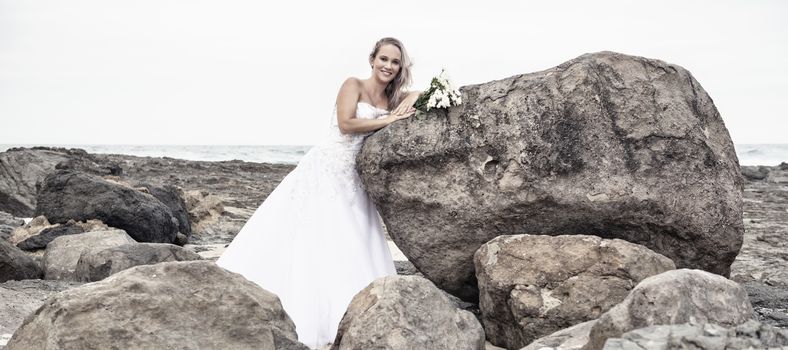 Beautiful bride at the beach with a flower bouquet.