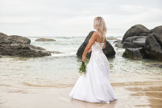 Beautiful bride at the beach with a flower bouquet.