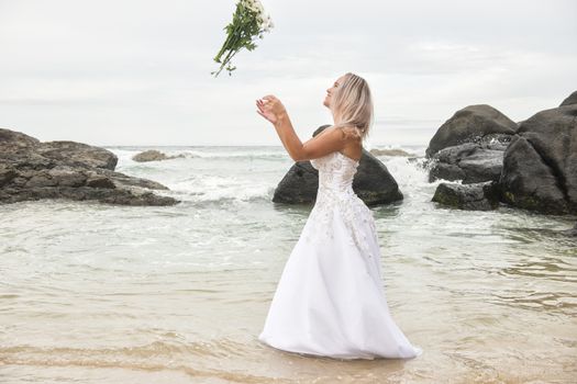 Beautiful bride at the beach with a flower bouquet.