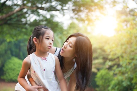 Mother embracing daughter in the park , Asian family outdoor lifestyle, morning with sun flare.