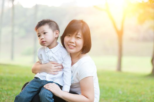 Mother hugging son in the park, Asian family outdoor lifestyle, morning with sun flare.