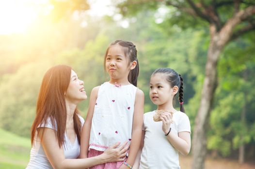 Happy mother and daughters laughing together outdoors. Family outdoor fun, morning with sun flare.