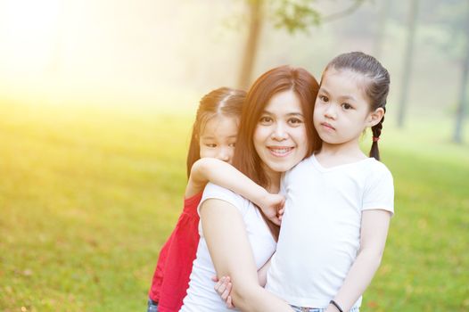 Lifestyle portrait Asian mother and daughter hugging in love at the outside in the park. Family outdoor fun, morning with sun flare.