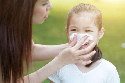 Mother helping daughter blow her nose at outside, in the park. Family outdoor lifestyle.