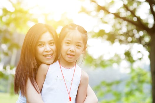 Mother and child are hugging and having fun outdoor in nature - photo with sun flare.