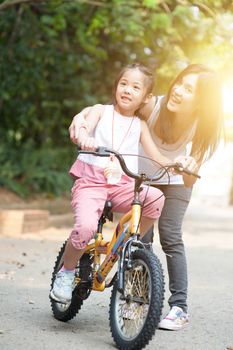 Little girl learning ride on bicycle with help of mother in the park, Asian family outdoor fun activity.