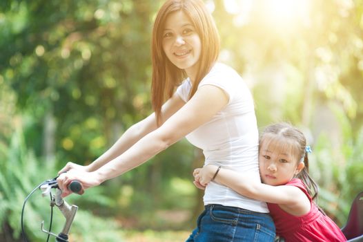 Mother and daughter riding bicycle in garden park, Asian family outdoor fun activity.