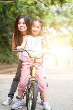 Asian mother and daughter riding bicycle in the park, family outdoor fun activity.