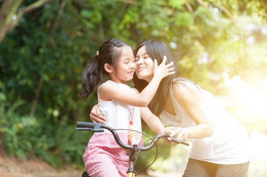 Little girl biking in the park, mother giving a goodbye kiss , Asian family outdoor fun activity.