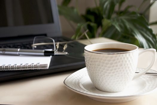 Blank notepad over laptop and coffee cup. Work desk with laptop computer and hot coffee cup with defocused background