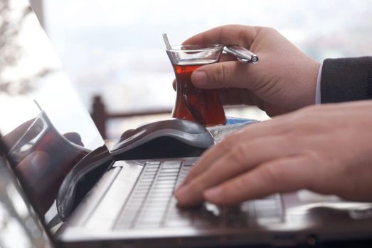 Close-up view of the hands on the keyboard while working and drinking tea with a businessman laptop.