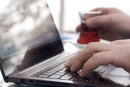 Close-up view of the hands on the keyboard while working and drinking tea with a businessman laptop.