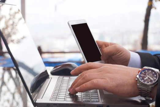 Businessman is checking his smartphone while working on his laptop.