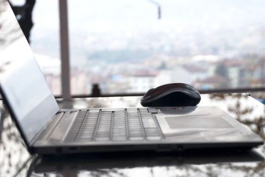 Laptop computer on a glass table at the window.