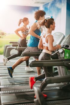 Three young friends  jogging on treadmills at the gym.