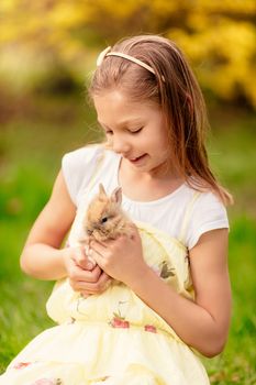 Beautiful smiling little girl holding cute bunny on nature in spring holidays.
