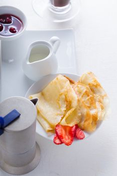 Crepes with strawberries and coffee on a white surface