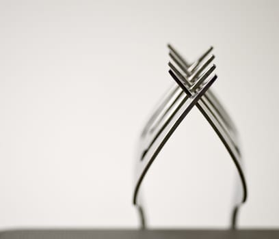 Tines of two forks intertwined/balanced with isolated white background.
