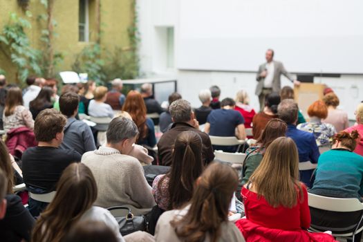 Male speaker giving presentation in lecture hall at university workshop. Audience in conference hall. Rear view of unrecognized participant. Scientific conference event. Copy space on whitescreen.