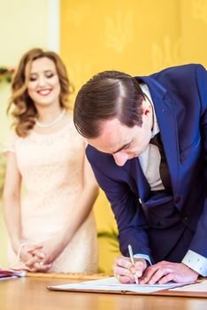 Gorgeous bride and groom signing wedding certificate at the registry office in Lviv, Ukraine