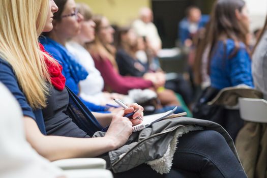 Female hands holding pens, notebook and phone and making notes at conference lecture. Event participants in conference hall.