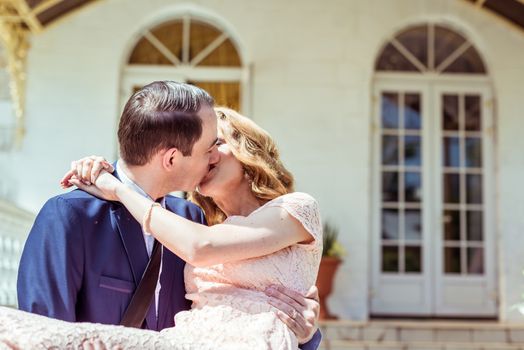 Groom holding bride in his arms and kissing after the ceremony at the registry office in Lviv, Ukraine