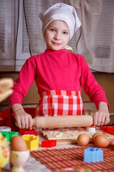 Cute girl in apron making easter cookies in kitchen