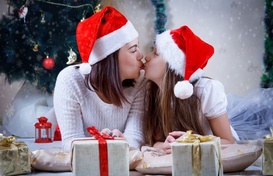 Mother and daughter kissing under Christmas tree