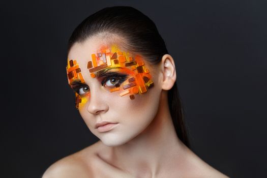 Portrait of a girl with an original make-up. Beauty close-up with orange and red rhinestones on a face of the model