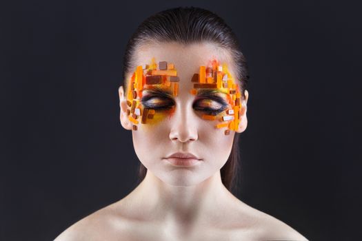 Portrait of a girl with an original make-up. Beauty close-up with orange and red rhinestones on a face of the model